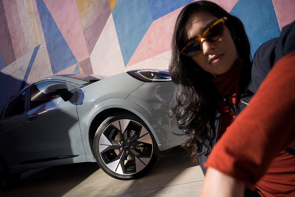 Una persona sentada junto a un coche Ford Puma híbrido suave plateado.