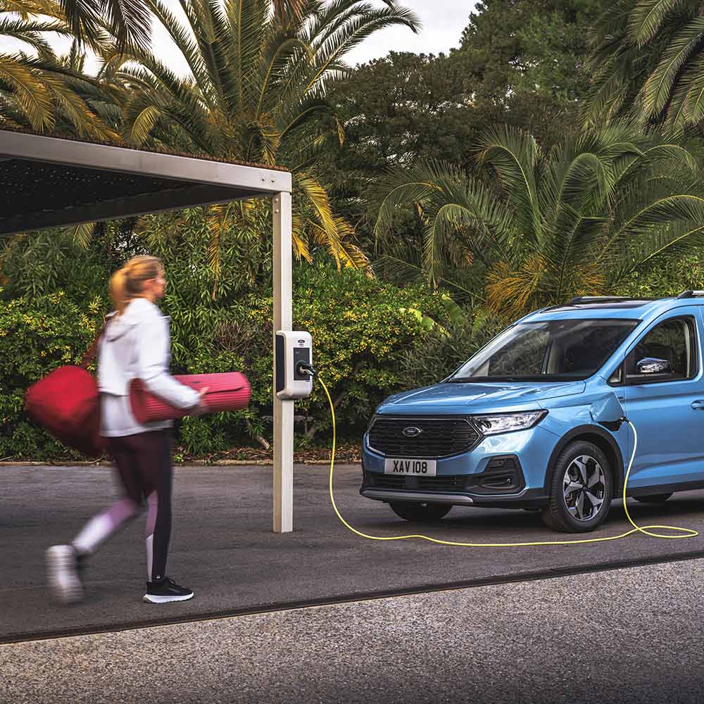 Una persona con una colchoneta de yoga caminando hacia una furgoneta híbrida enchufable Ford Tourneo Connect.