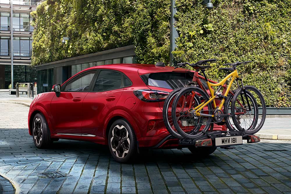Ford Puma rojo aparcado en un entorno urbano con dos bicicletas en un portabicicletas trasero.