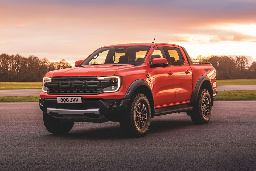 Una camioneta pick-up Ford Ranger Raptor naranja aparcada en un paisaje pintoresco.