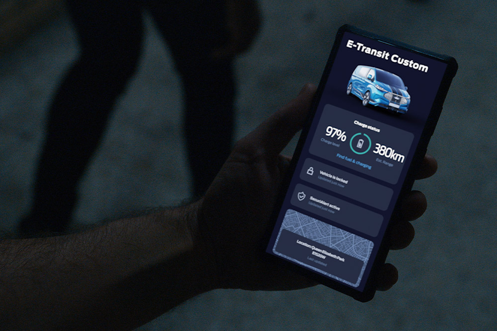 Teléfono inteligente que muestra una E-Transit Custom en la aplicación FordPass, indicando el estado de carga del vehículo y su ubicación.