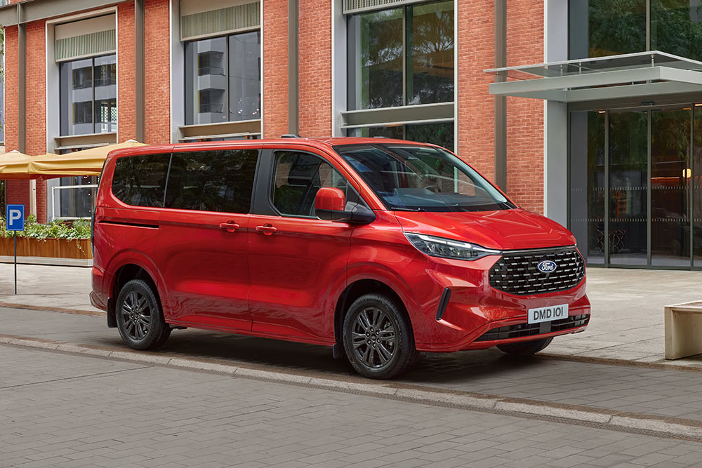 Una Ford Tourneo Custom roja aparcada en una calle de la ciudad frente a un edificio de ladrillo