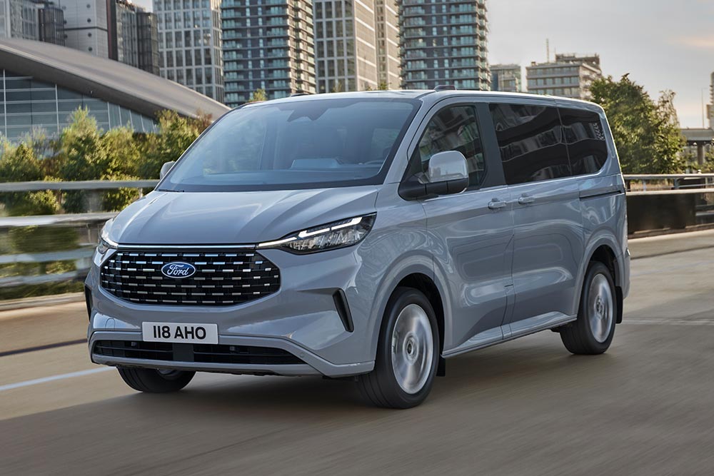 Un Ford Tourneo Custom plateado que recorre una calle urbana.