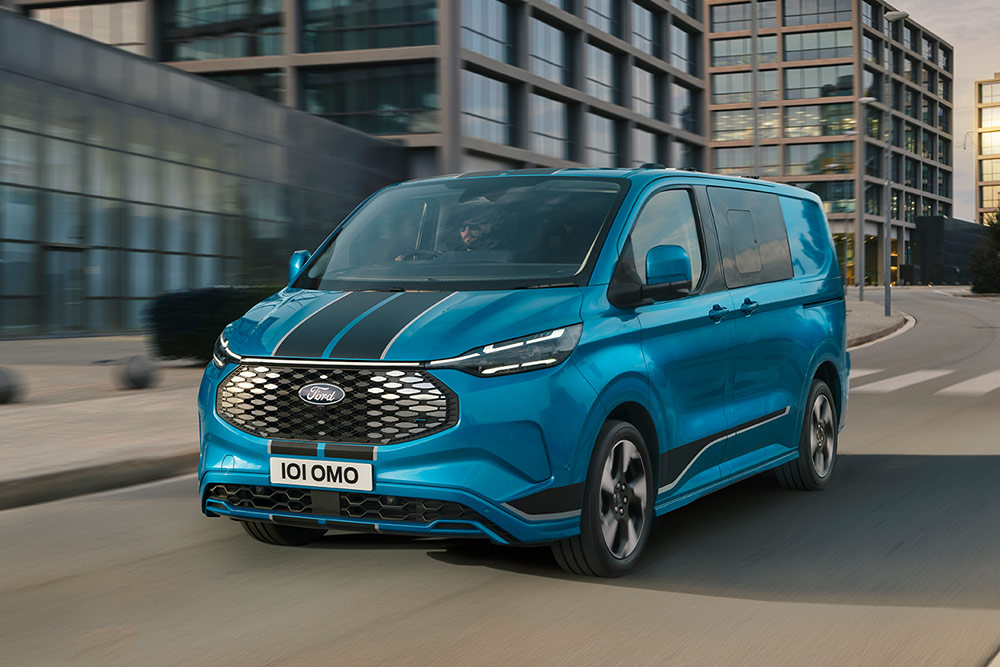 Una furgoneta Ford E-Transit Custom Sport azul con doble cabina recorriendo una calle de una ciudad.