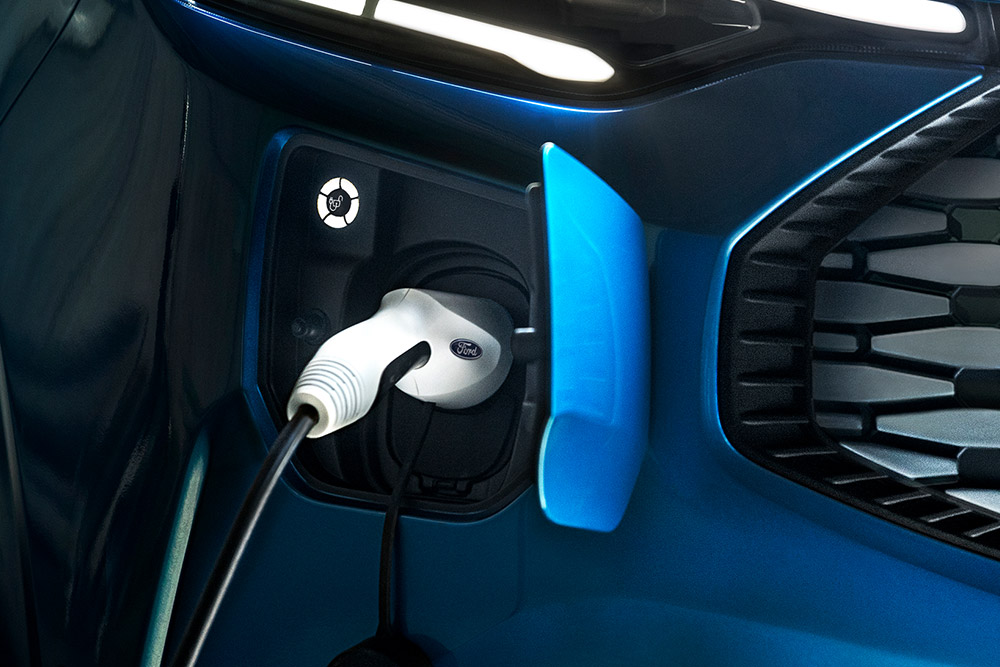 Primer plano de un puerto de carga en una furgoneta eléctrica Ford E-Transit azul con un cable de carga enchufado.