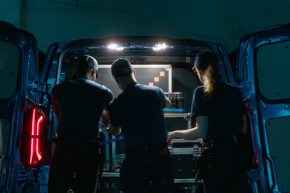 Tres personas trabajando en la parte trasera de una furgoneta Ford E-Transit Custom.