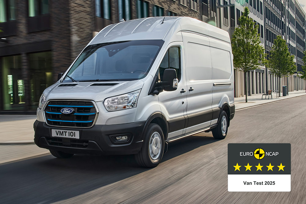 Furgoneta eléctrica Ford E-Transit plateada circulando por una carretera con la insignia «Gold 2022 Commercial Van Safety».