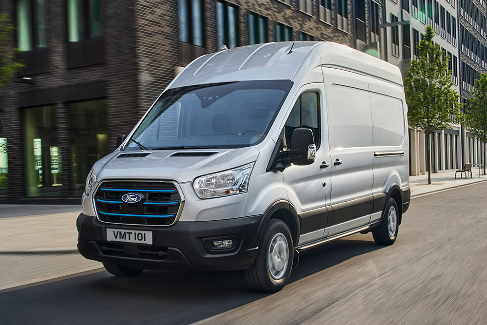 Furgoneta eléctrica Ford E-Transit plateada circulando por una calle de la ciudad.