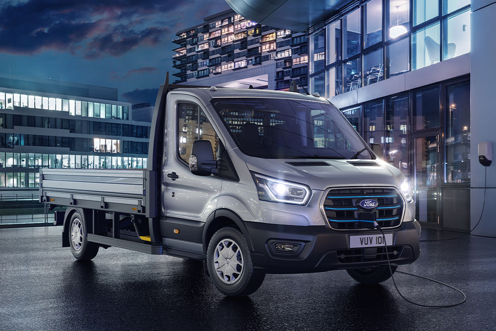 Una Ford E-Transit Chasis Cabina plateada estacionada frente a un edificio moderno por la noche.