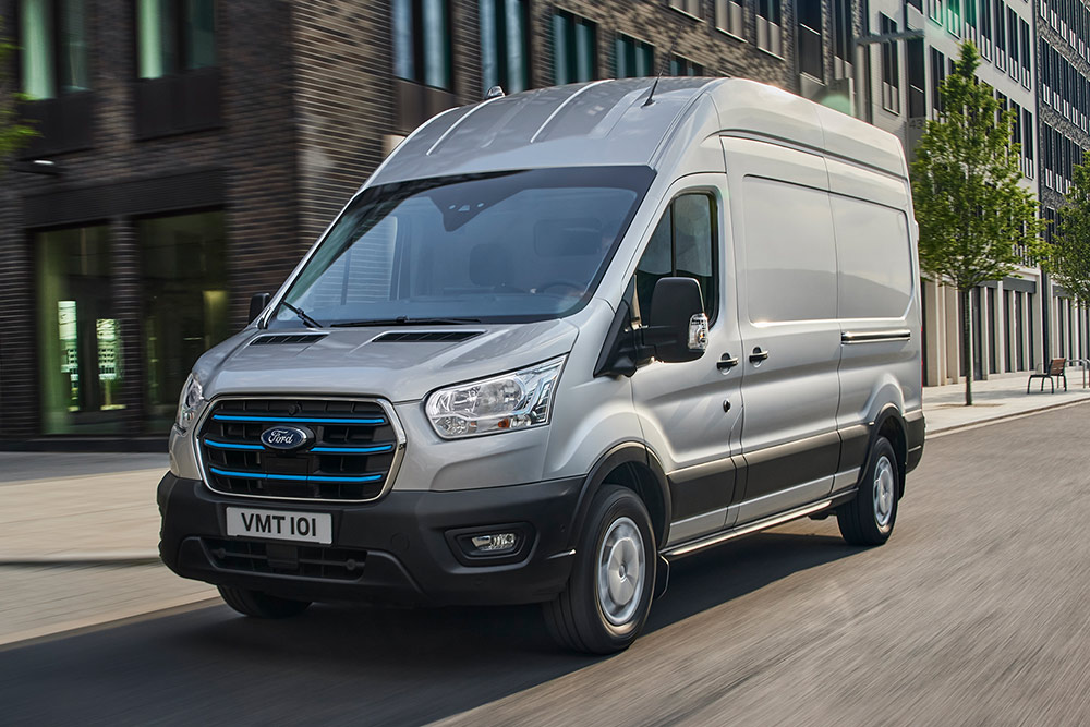 Un Ford Transit plateado circulando por un paisaje urbano.