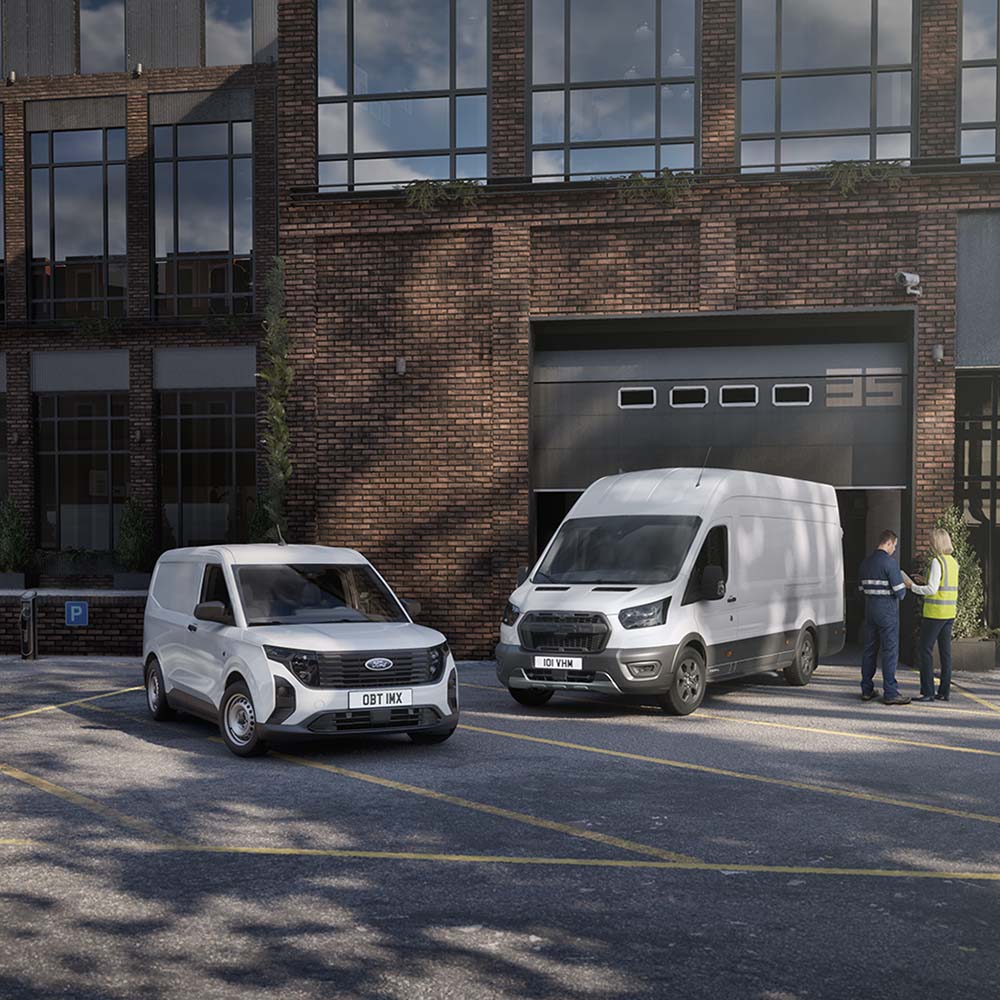 Dos furgonetas Ford blancas estacionadas frente a un edificio moderno mientras dos personas conversan junto a los vehículos.