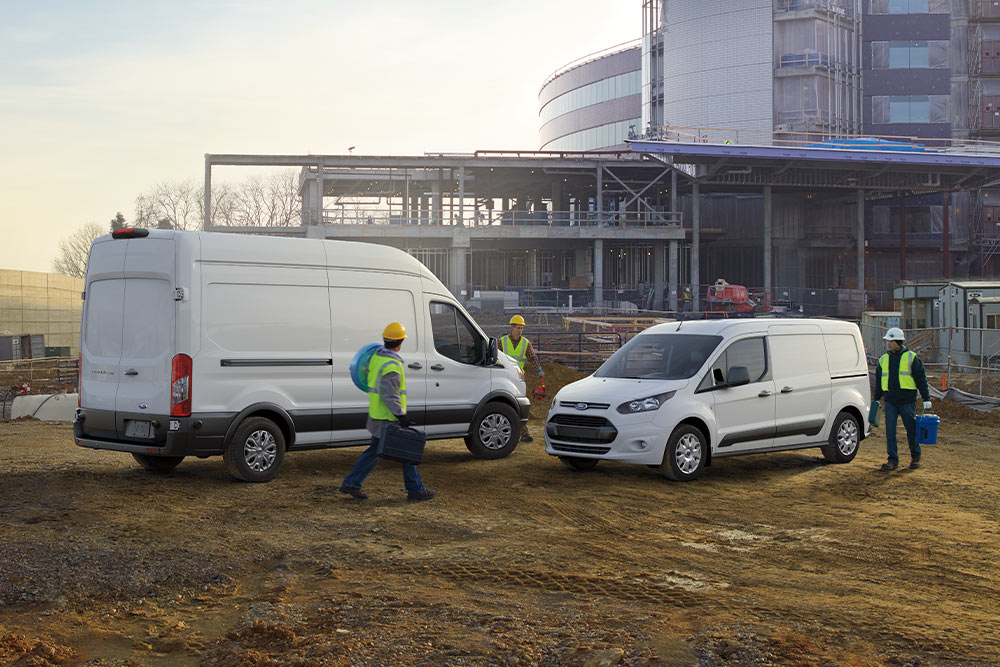  Dos furgonetas Ford blancas aparcadas en una obra con trabajadores caminando alrededor.