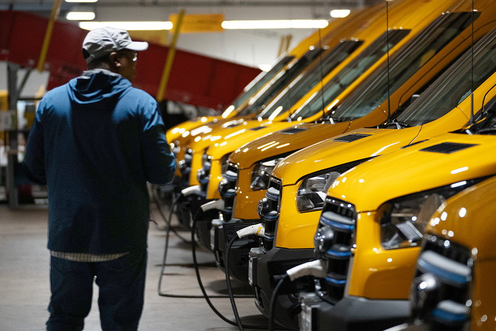  Una fila de furgonetas eléctricas Ford amarillas siendo cargadas, un hombre está de pie junto a ellas.