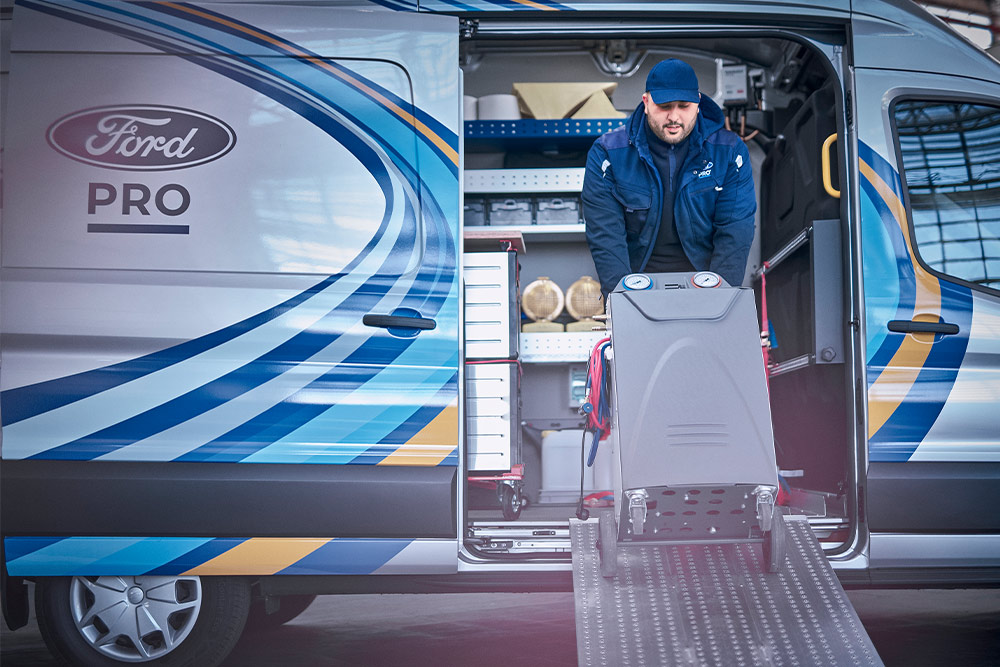 Un técnico móvil de Ford Pro sacando herramientas de una furgoneta Transit delante de un negocio.