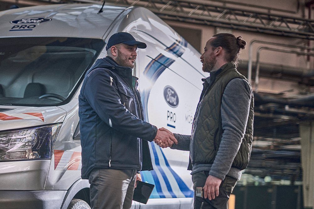 Un técnico de Ford Pro habla con un cliente, con una furgoneta Ford Pro Mobile Service visible al fondo.