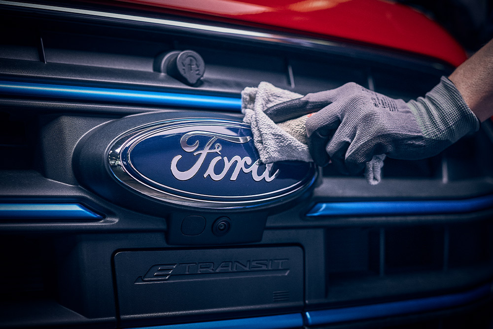 Primer plano de un técnico puliendo el logotipo de Ford en la parte delantera de una furgoneta roja.