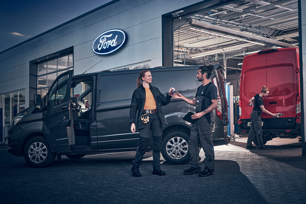 Cliente y técnico de Ford intercambiando llaves de una furgoneta frente a un concesionario Ford.