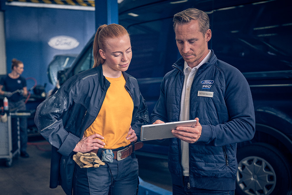 Técnico de Ford y gerente de flota revisando datos en una tablet en un garaje.