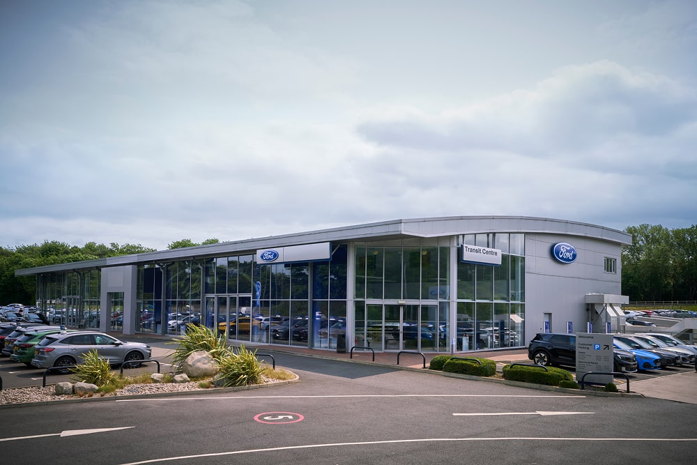 Vista exterior de un concesionario de coches Ford con grandes ventanales. Aparecen coches aparcados fuera.